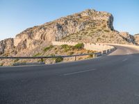 road going through mountain landscape with large rock formation in distance on hilltop side of roadway