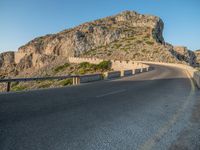 road going through mountain landscape with large rock formation in distance on hilltop side of roadway