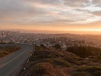 the view of a road running through a city skyline towards the horizon at sunset with a winding curve