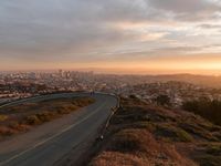 the view of a road running through a city skyline towards the horizon at sunset with a winding curve