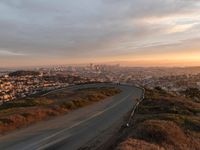 the view of a road running through a city skyline towards the horizon at sunset with a winding curve