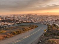 the view of a road running through a city skyline towards the horizon at sunset with a winding curve