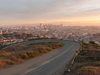 the view of a road running through a city skyline towards the horizon at sunset with a winding curve