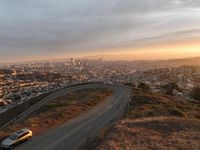 the view of a road running through a city skyline towards the horizon at sunset with a winding curve