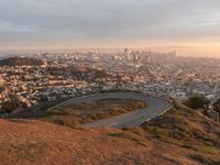 the view of a road running through a city skyline towards the horizon at sunset with a winding curve