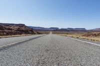 the road that runs into the desert is empty and a bright blue sky is visible in the background