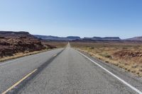 the road that runs into the desert is empty and a bright blue sky is visible in the background