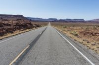 the road that runs into the desert is empty and a bright blue sky is visible in the background