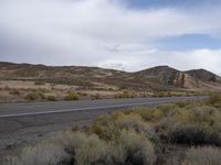 a road in the middle of the desert near a mountain range with trees and shrubs