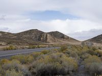 a road in the middle of the desert near a mountain range with trees and shrubs