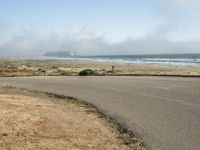 the road leads to an empty beach where two people are sitting and a person is standing near the water