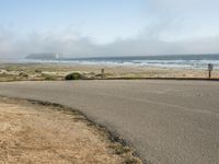 the road leads to an empty beach where two people are sitting and a person is standing near the water