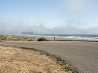 the road leads to an empty beach where two people are sitting and a person is standing near the water