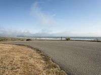 the road leads to an empty beach where two people are sitting and a person is standing near the water