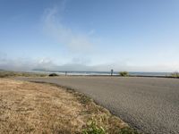 the road leads to an empty beach where two people are sitting and a person is standing near the water