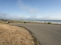 the road leads to an empty beach where two people are sitting and a person is standing near the water