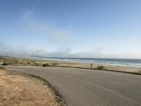 the road leads to an empty beach where two people are sitting and a person is standing near the water