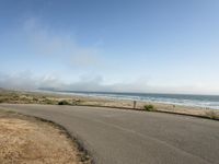 the road leads to an empty beach where two people are sitting and a person is standing near the water