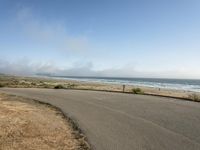 the road leads to an empty beach where two people are sitting and a person is standing near the water