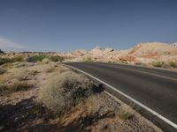 road leading to a red rock area in the desert under a clear sky with no clouds