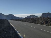 a lone person riding a motorcycle along a road next to a mountain range with mountains