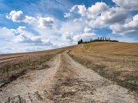 a dirt road with grass on either side of it leads up to a grassy hill in the distance