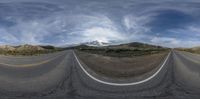 a street in the middle of a desert with clouds above and mountains behind it that have white lines on the ground