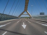 a truck driving across a bridge near a street corner near buildings and a bridge with many cables