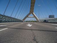 a truck driving across a bridge near a street corner near buildings and a bridge with many cables