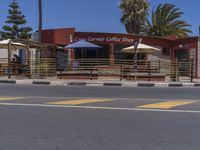 a small cafe and restaurant are on a roadside road near palm trees and buildings with umbrellas