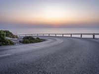 a person standing on the side of a winding road over looking the ocean at sunset