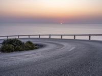 a person standing on the side of a winding road over looking the ocean at sunset