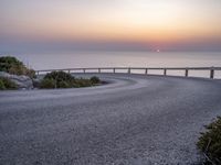 a person standing on the side of a winding road over looking the ocean at sunset