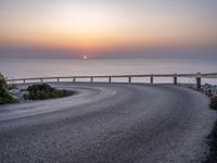 a person standing on the side of a winding road over looking the ocean at sunset