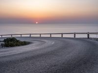 a person standing on the side of a winding road over looking the ocean at sunset