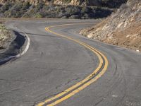 the empty roadway with curve in the middle is very steep terrain and mountain views appear to be in the background