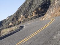 the empty roadway with curve in the middle is very steep terrain and mountain views appear to be in the background