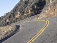 the empty roadway with curve in the middle is very steep terrain and mountain views appear to be in the background