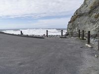 a road going past a rock beach with waves coming in to the shore area and a person walking along the side