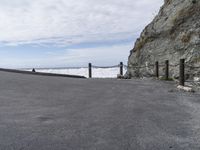 a road going past a rock beach with waves coming in to the shore area and a person walking along the side