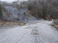 a dirty paved roadway with a rock cliff behind it and a bridge over it that has not yet been built