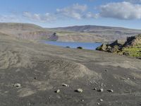 a rock covered beach surrounded by hills under a blue sky on a windy day's day