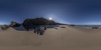 sand on the beach and large rock formation near the ocean with the sun rising behind