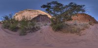 a rock formation with a tree on top of it in the desert near a hill and a dirt area with a sky background