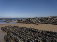 a beach with rocks and seawater on the shoreline below it is clear blue sky