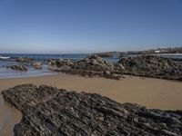 a beach with rocks and seawater on the shoreline below it is clear blue sky