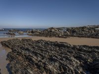 a beach with rocks and seawater on the shoreline below it is clear blue sky