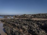 a beach with rocks and seawater on the shoreline below it is clear blue sky