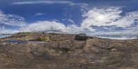 the rocks on a beach are under a partly cloudy sky with a small puddle near the rocks and ocean