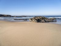 a large rock is on a beach next to the water and sand area, as if its in ocean